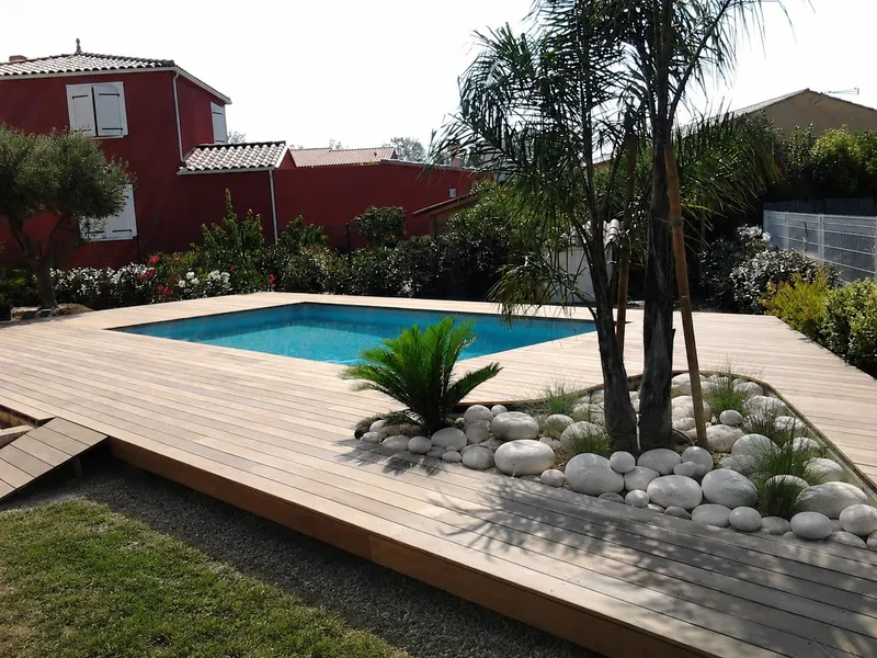 Plage de piscine en bois avec massif de galets et palmier intégré