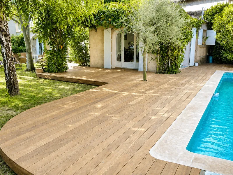 Grande terrasse bois entourant une piscine devant un mas provençal, avec olivier intégré